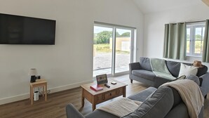 Una sala de estar moderna con un televisor de pantalla plana, una mesa de centro de madera, un sofá gris y una ventana con cortinas.