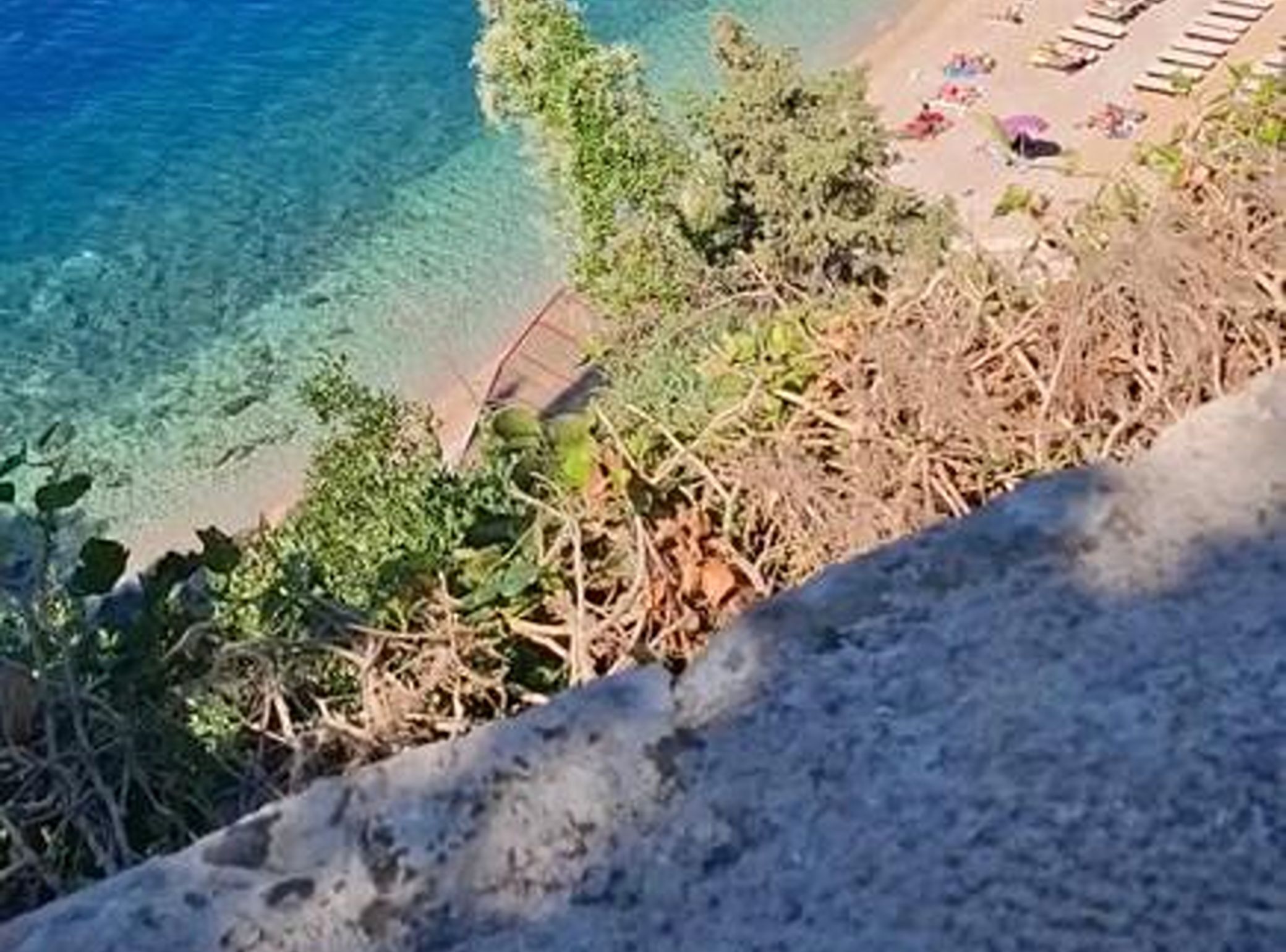 Una playa con agua cristalina, algunas sombrillas y vegetación.