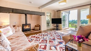 Een gezellige woonkamer met een open haard, een flatscreen televisie en een groot raam met uitzicht op de omgeving.