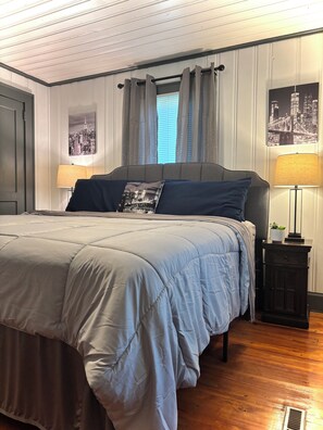 Una camera da letto con un letto, tende, un comodino, una lampada e una fotografia con vista sulla città.