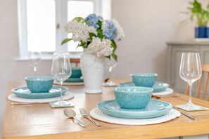 Une table à manger dressée avec des bols, des assiettes et des verres à vin bleus, et un vase de fleurs en arrière-plan.