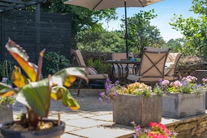 Eine Terrasse im Freien mit Tisch und Stühlen, umgeben von Blumentöpfen und Blumen.