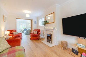 A living room with a fireplace, red sofas, a TV, and a dining area with a table and chairs. - 4 Bed in Southwold (oc-t42835) (Southwold)