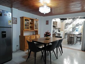 Une cuisine avec des meubles de rangement en bois, une table à manger avec des chaises, un réfrigérateur et un lustre.