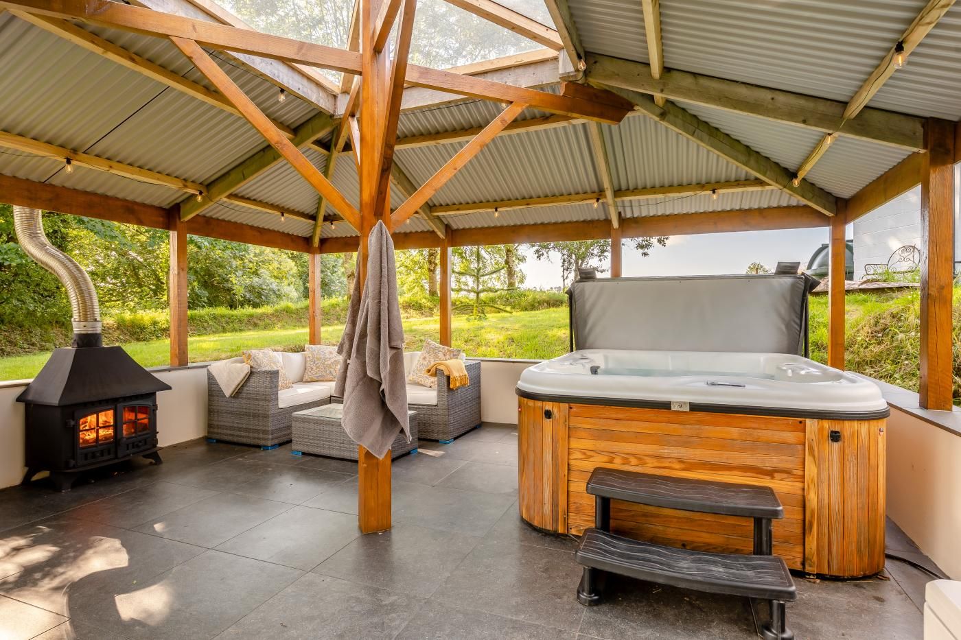 A covered outdoor area with a hot tub, a wood-burning stove, and outdoor seating.