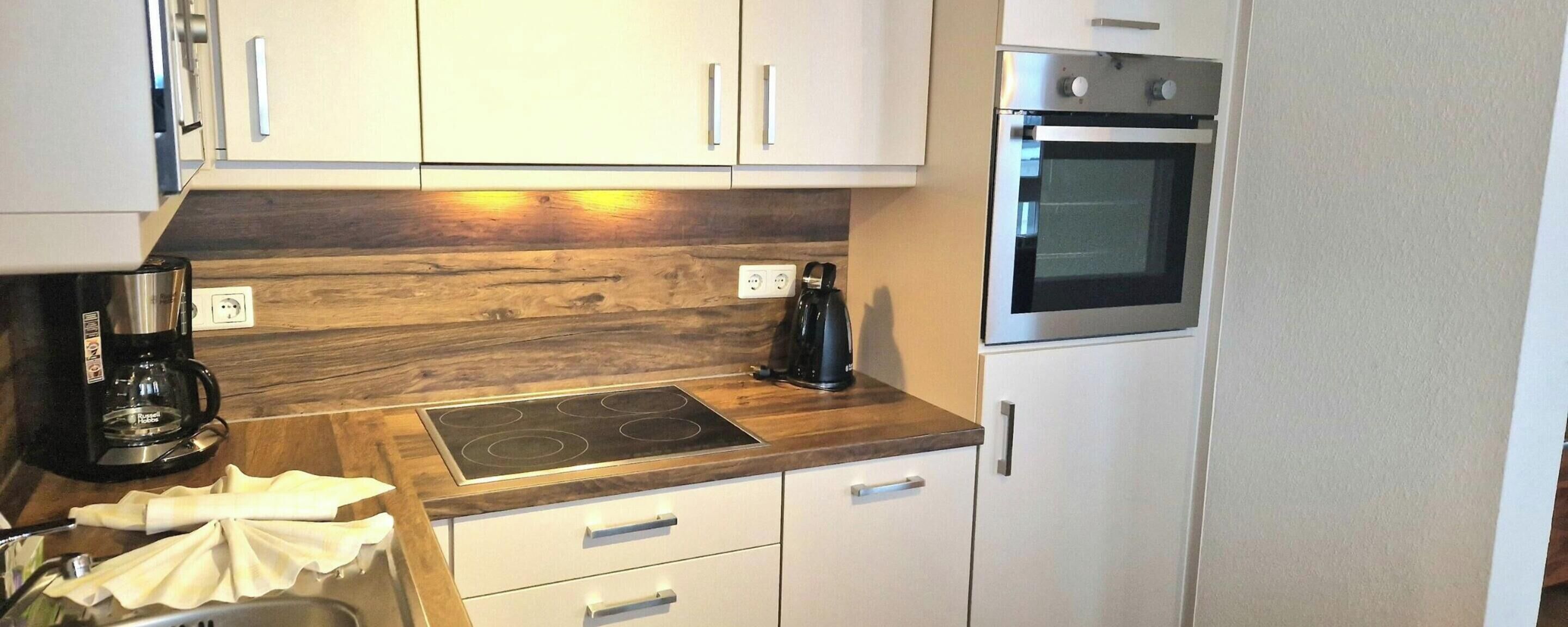 Eine kleine Küche mit weißen Schränken, einer Holz Arbeitsplatte, einem eingebauten Herd und einem Edelstahlbackofen.