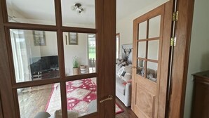 Una porta de fusta amb panells de vidre, que dona pas a un saló amb una catifa vermella, un sofà i una televisió.