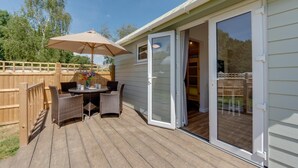 Una terraza con mesa y sillas, cerca viva de madera, y un ventanal corredizo que da a un espacio interior.