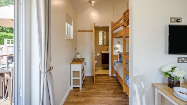 Un couloir étroit avec un plancher en bois, une armoire blanche avec des paniers en osier, un lit superposé et un téléviseur fixé au mur.