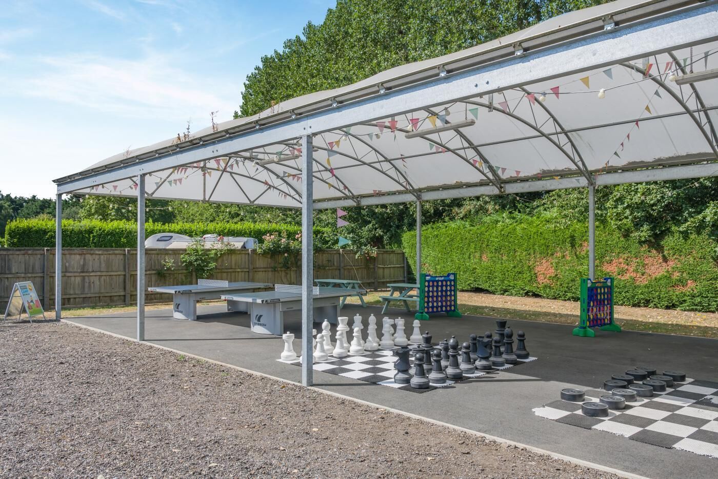 An outdoor chess setup under a covered pavilion with picnic tables and a chessboard.