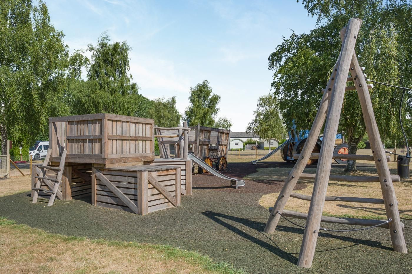 Ein Spielplatz mit Holzspielgeräten, darunter eine Rutsche und Kletterbereiche.