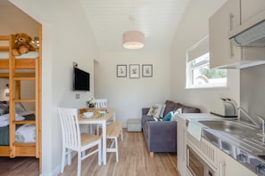 A compact living space with a bunk bed, a dining area with a table and chairs, a sofa, a kitchen with a sink and stove, and a television mounted on the wall.