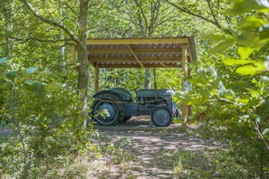 A vintage tractor parked under a wooden shelter in a wooded area.