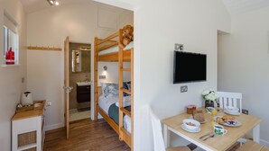 Un dormitorio con literas, una mesita de noche con lámpara, un televisor montado en la pared y una mesa de desayuno con comida y bebidas.