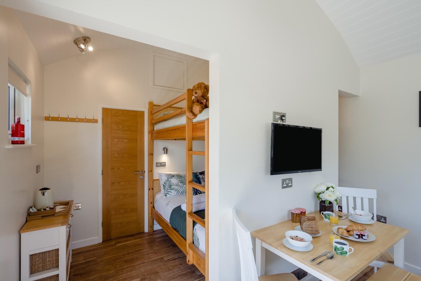Habitación pequeña con una cama individual, una mesita con alimentos para el desayuno, un televisor en la pared y una puerta de madera.