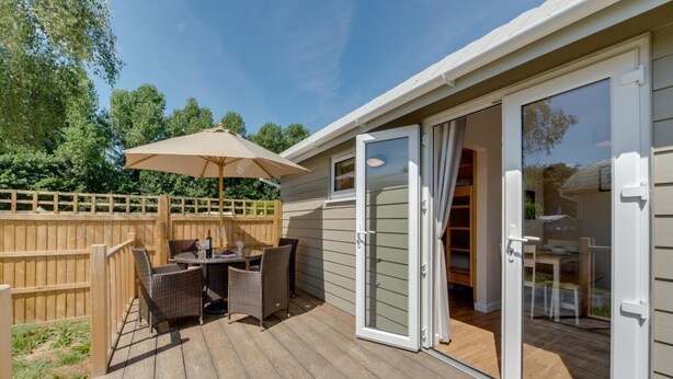 Um deck com mesa e cadeiras, cerca de madeira e porta de vidro deslizante que dá para o interior.
