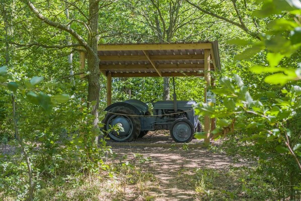 A vintage car parked under a wooden shelter in a wooded area.