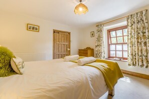 Ein Schlafzimmer mit einem großen Bett, einer Holztür, einem Schminktisch und einem Fenster mit blumigen Vorhängen.