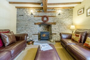Un salon chaleureux avec des murs en pierre, une cheminée, des canapés en cuir et un tapis.