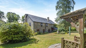 A stone building with a thatched roof, surrounded by a well-maintained lawn and a wooden fence. - 4 Bed in Newchurch (oc-bow333) (Newchurch)
