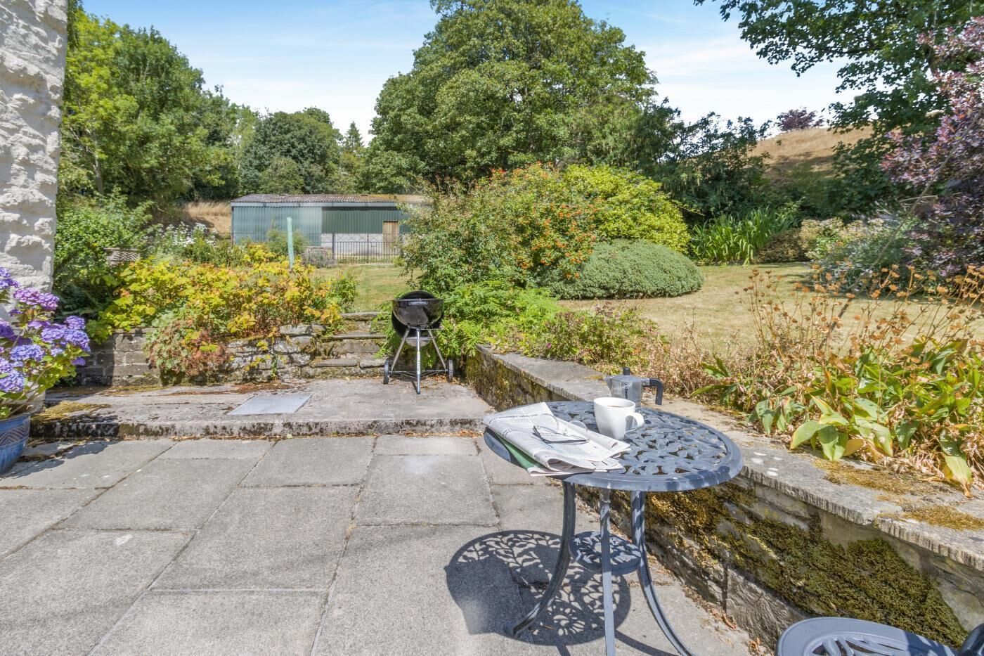 A patio with a grill, a table with a cup and newspaper, and a stone wall.