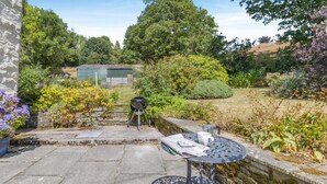 A patio with a grill, a table with a cup and newspaper, and a stone wall. - 4 Bed in Newchurch (oc-bow333) (Newchurch)