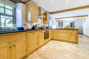 A spacious kitchen with wooden cabinets, a large island, and a view to the dining area. - 4 Bed in Newchurch (oc-bow333) (Newchurch)