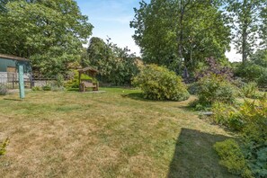 Ein Garten mit einem hölzernen Gartenpavillon, einem eingezäunten Bereich und verschiedenen Sträuchern und Bäumen.