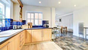 Een moderne keuken met houten kastjes, een blauwe betegelde spatwand en een eethoek met tafel en stoelen.
