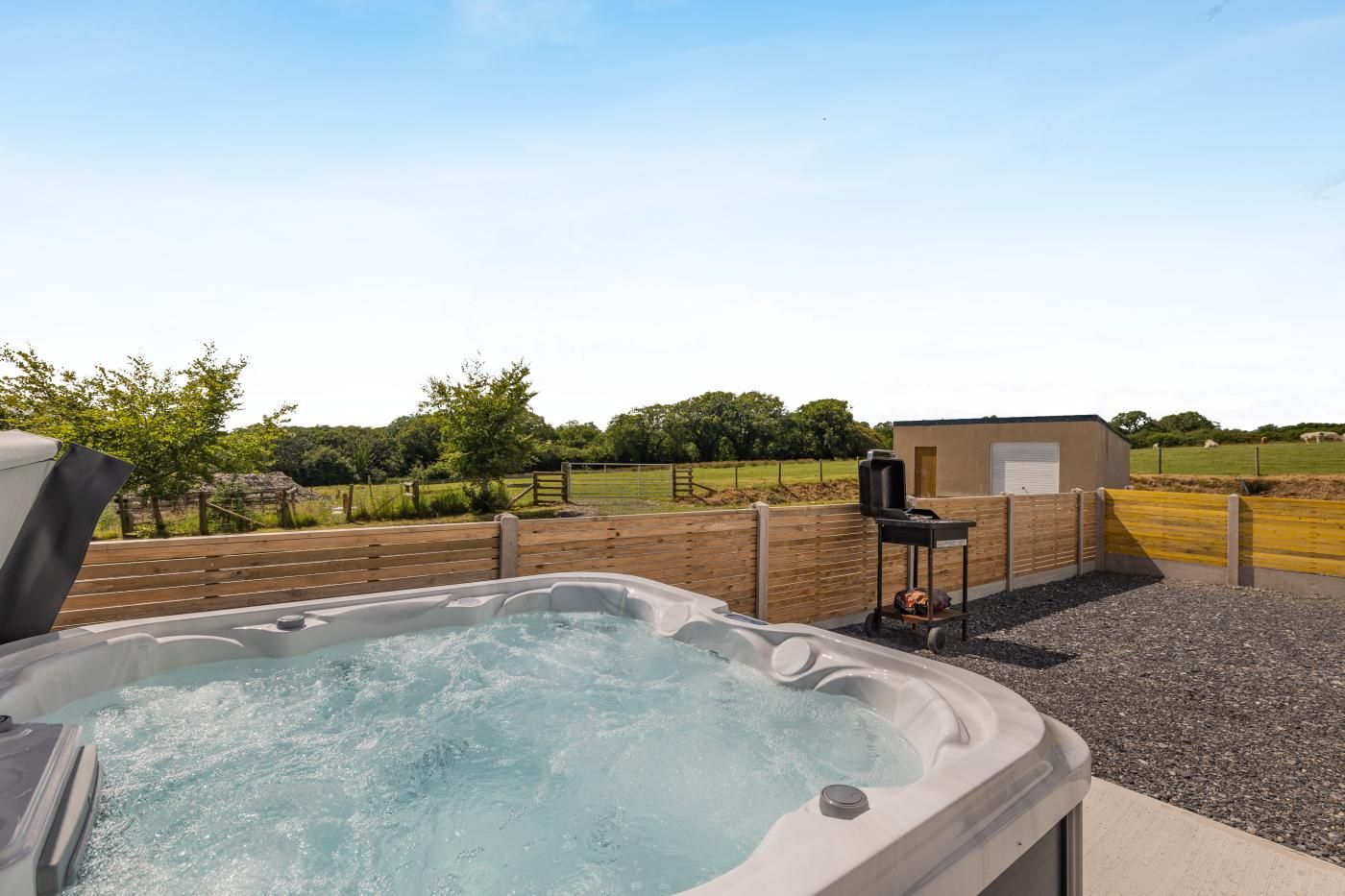 A hot tub with a wooden deck and a barbecue grill in the background.