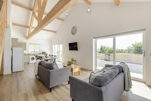 A spacious living area with a kitchen in the background, a large window, and a flat-screen TV mounted on the wall. - 6 Bed in Meidrim (oc-b45396) (Meidrim)