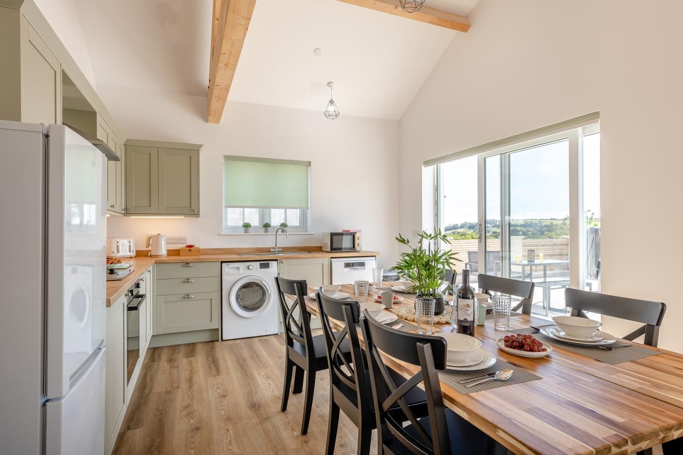Una cocina moderna con lavadora integrada, suelo de madera y zona de comedor con vistas al exterior.
