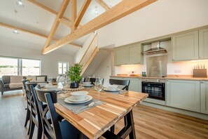 A modern kitchen with light green cabinets, a stainless steel range hood, and a wooden dining table set for four. - 6 Bed in Meidrim (oc-b45396) (Meidrim)