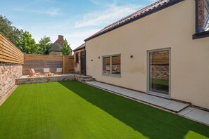 Ein Garten mit Kunstgrashalm, Holzlattenzaun und Ziegelmauer.