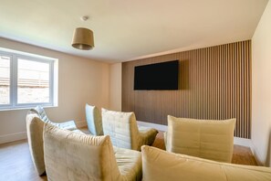 Ein modernes Wohnzimmer mit Flachbildfernseher an einer Wand aus Holzpaneelen, einem großen Fenster und einer Deckenleuchte.