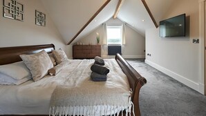 Un dormitorio con techo inclinado, cama, cómoda, televisor y ventana.