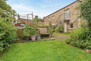 A stone building with a garden area featuring potted plants and a wooden bench. - 2 Bed in Thornton Rust (oc-t45331) (Thornton Rust)