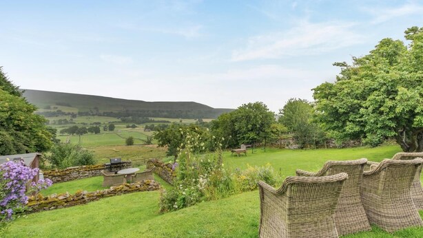 A grassy outdoor area with wicker furniture, a stone wall, and a view of rolling hills. - 2 Bed in Thornton Rust (oc-t45331) (Thornton Rust)