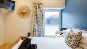 Une chambre d’hôtel avec un lit, un bureau, une télévision, une décoration murale en forme de soleil et une fenêtre avec des rideaux.