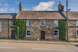 Un bâtiment en pierre de deux étages, avec une porte marron foncé, des fenêtres à cadre blanc et un toit en briques.