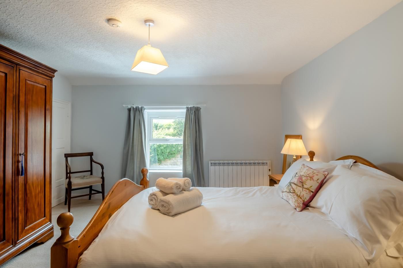 Quarto com cama, cadeira, guarda-roupa, janela com cortinas e radiador.