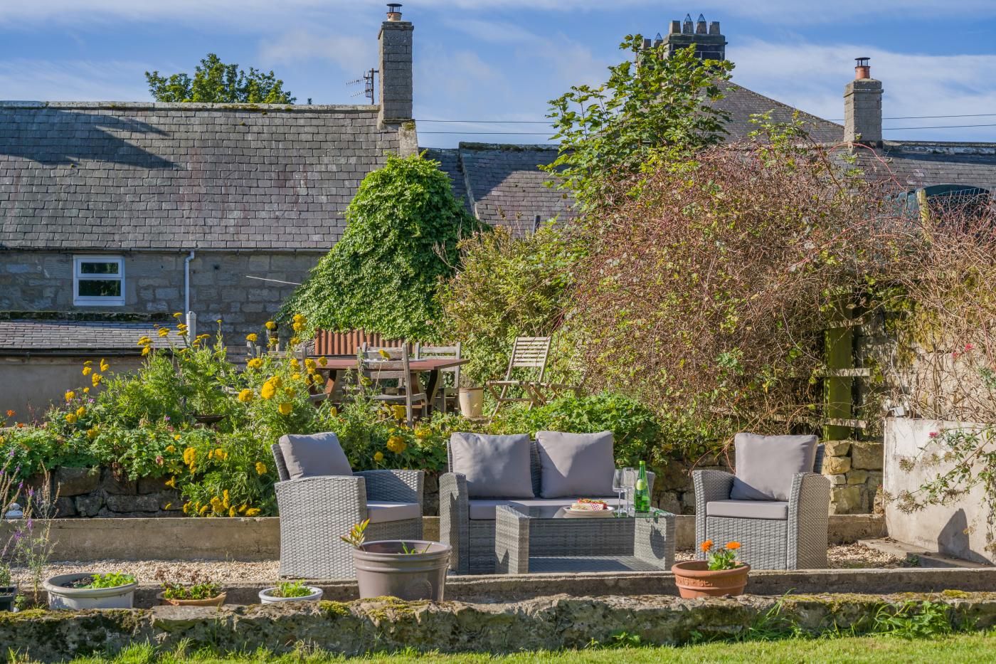 A garden with outdoor furniture, a stone wall, and a house with a tiled roof.