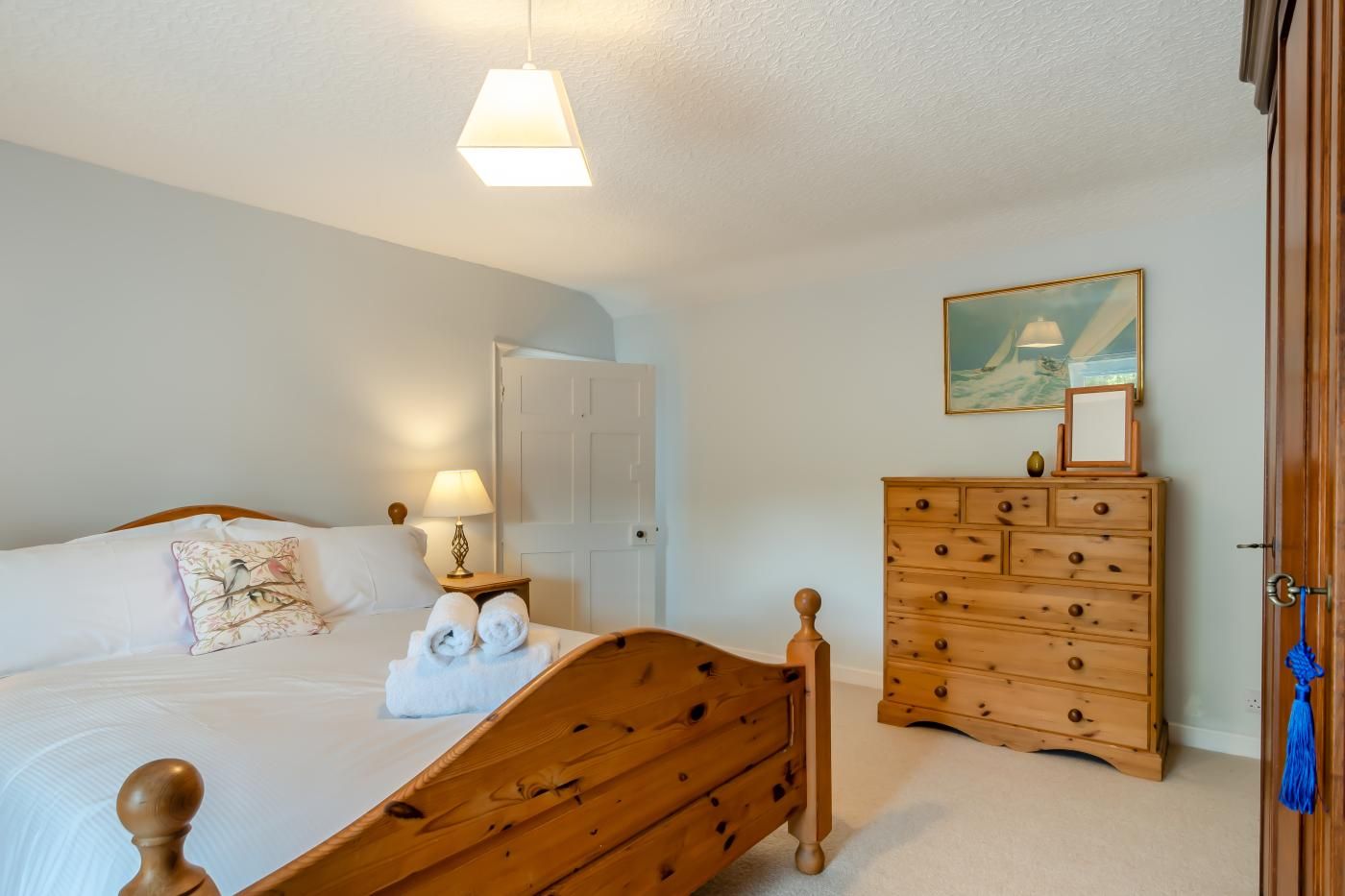 Une chambre à coucher avec un lit en bois, une table de chevet avec une lampe, une commode et un tableau accroché au mur.