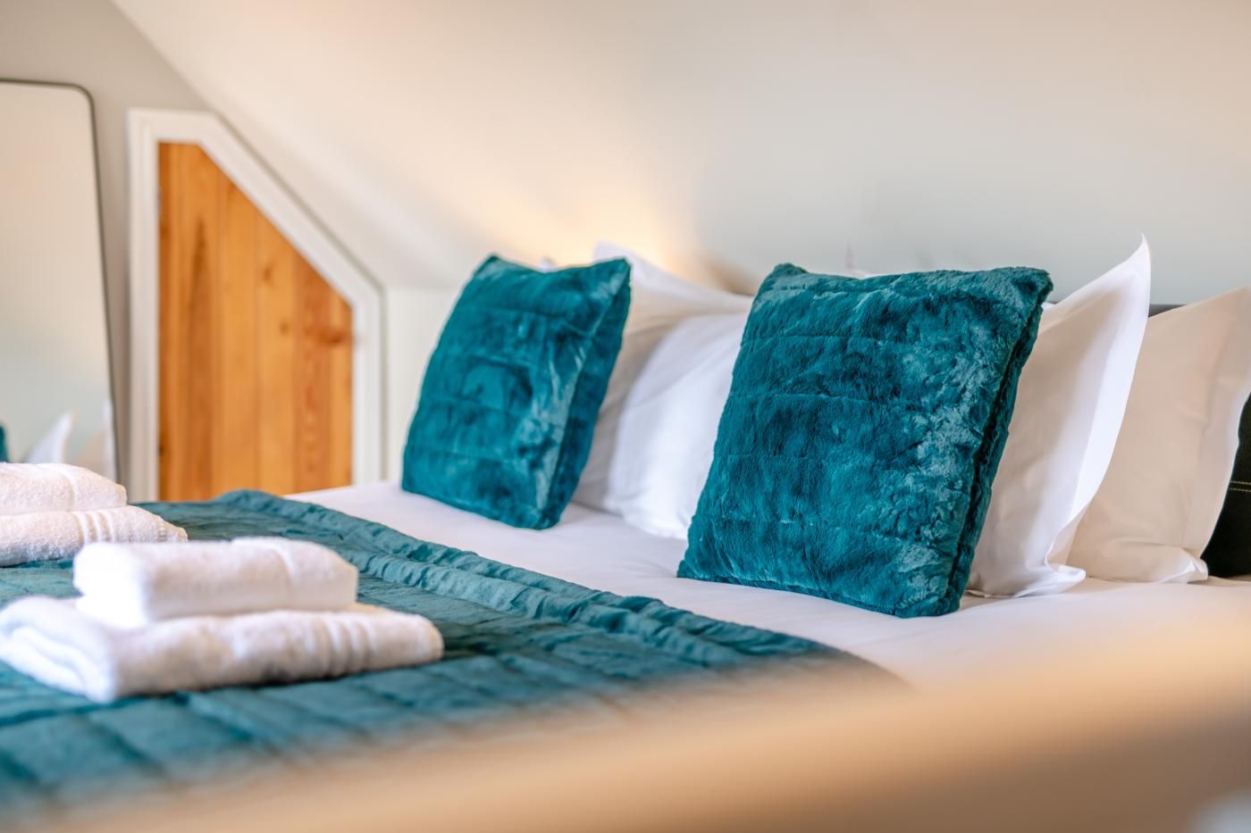Un lit bien fait, avec des oreillers turquoise et blancs, une couvre-lit turquoise et des serviettes blanches.