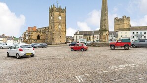 A cobblestone square with historic buildings, a clock tower, and a tall monument.