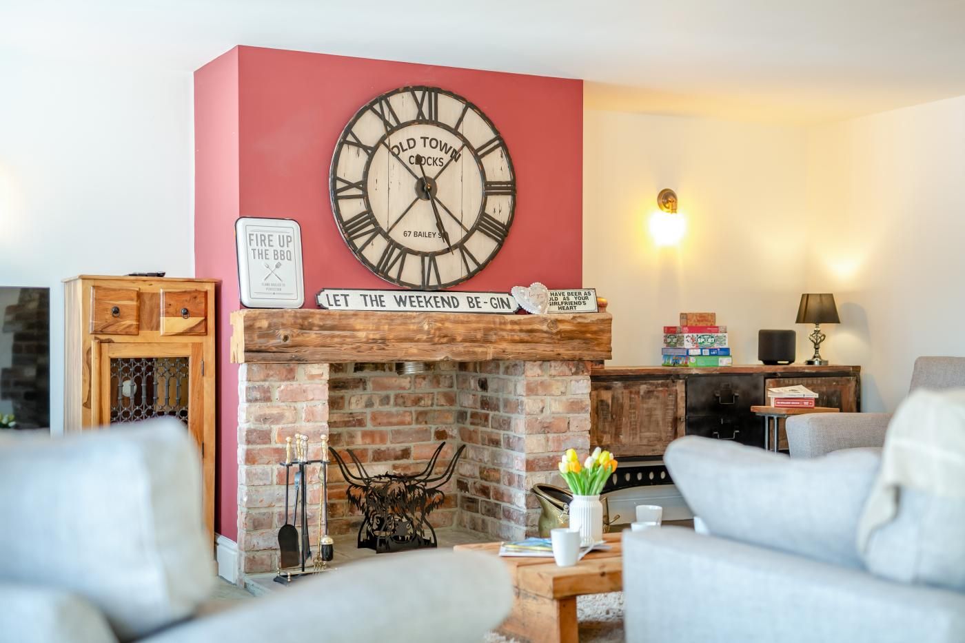 A living room with a brick fireplace, a large clock, and a sign that reads 'LET THE WEEKEND BE - GIN'.