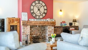 A living room with a brick fireplace, a large clock, and a sign that reads 'LET THE WEEKEND BE - GIN'. - 4 Bed in Scorton (oc-t44226) (Scorton)