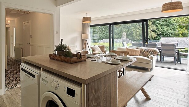 Une cuisine moderne dotée d’un lave-linge intégré, d’un îlot central en bois et d’un coin repas offrant une vue sur l’extérieur.
