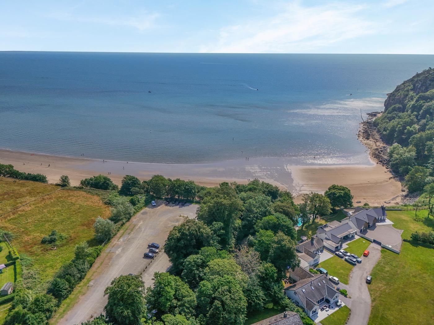 An aerial view of a coastal property with a beach, parking area, and residential buildings.