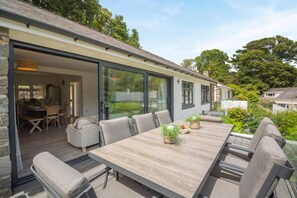 Ein modernes Haus mit einer großzügigen Terrasse, komplett mit Esstisch, Stühlen und Blumentöpfen.